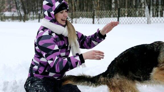 一个穿着冬季夹克的年轻女子在雪地里和一只德国牧羊犬玩耍