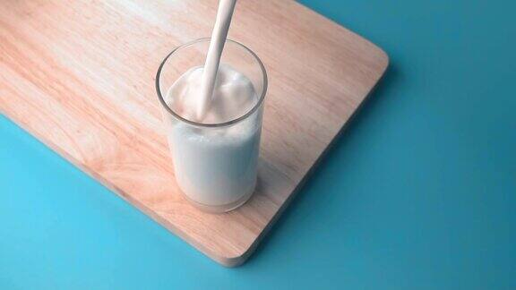 将牛奶从锅中倒入有木板和蓝色背景的玻璃中