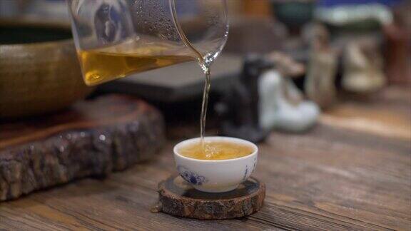 将泡好的茶从玻璃茶壶中倒入白色陶瓷杯中