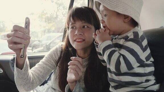 亚洲母亲和她的儿子在汽车后座用智能手机拍照
