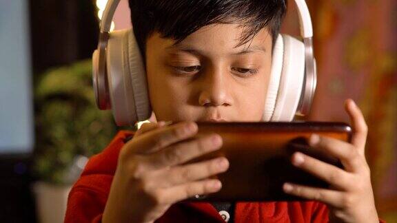 男孩戴着耳机在智能手机上玩游戏的照片