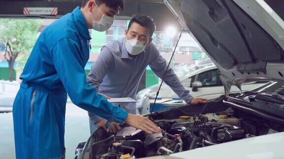 亚洲汽车技师听客户解释汽车状况在新冠肺炎疫情期间车辆服务经理戴着口罩在修车厂维修汽车发动机