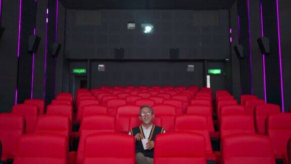 广角正面亚洲华人活跃的老人享受他的零食同时在电影院看电影电影院独自