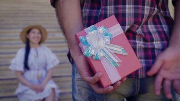 在户外小伙子背着礼盒给女朋友一个惊喜恋爱中的情侣为情人节或生日赠送礼物
