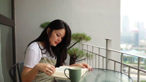 一个亚洲年轻女子在阳台上看书