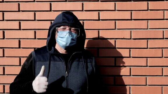 男士戴兜帽医用外科口罩安全防护专用封闭眼镜戴在脸上防护手套竖起大拇指表示病毒防护概念