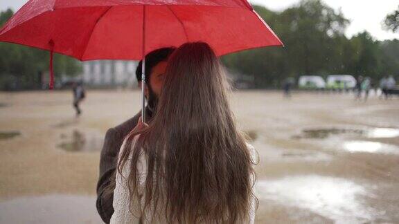 一对浪漫的年轻情侣在雨中撑着伞镜头在他们周围旋转