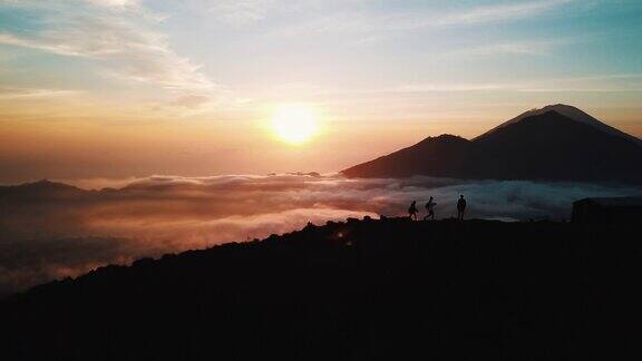 一群朋友跑上山站在巴图尔活火山山顶的云层之上在巴厘岛的日出空中拍摄4K