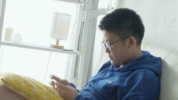 亚洲男孩戴着眼镜坐在家里的沙发上玩智能手机网络游戏生活方式概念