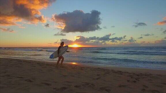 慢镜头:日落时分年轻的冲浪者在海滩上奔跑