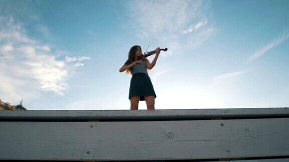 在夏日的蓝天下年轻女子拉着小提琴