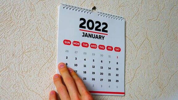 一个男人的手撕下挂在墙上的2022年日历扉页和1月页