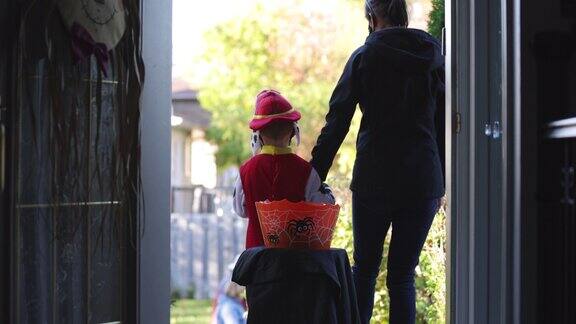 万圣节前夕一个小男孩戴着防护面具在家门口吃糖果