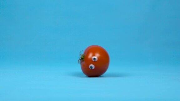 一个长着眼睛的红番茄在慢慢地滚动蓝色背景上的番茄卷缓慢的运动