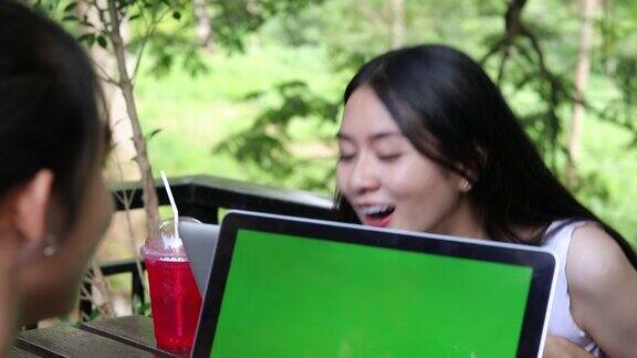 两个亚洲女人开心地笑着用笔记本电脑在咖啡店工作