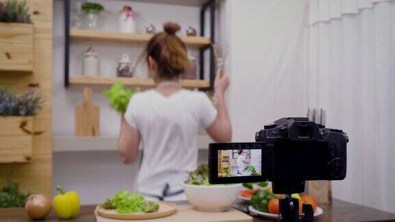 年轻的亚洲女性美食博主说话同时录制视频准备绿色沙拉在厨房教程视频到社交网络通过互联网在家概念选择性焦点