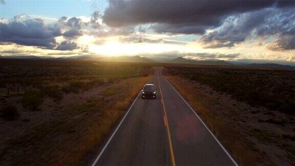 图片:金色的夕阳下一辆黑色SUV行驶在空旷的乡村道路上