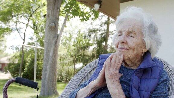 年长的白人基督教妇女与合十的手祈祷与她的眼睛闭在户外的草坪椅子在夏天