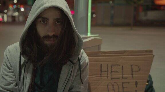 一个留着胡子和长发的无家可归的乞丐在空旷的街道上乞讨的慢动作他旁边的纸板上写着“帮助我”无家可归4k