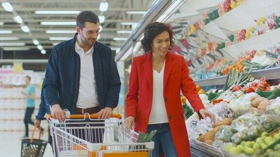 在超市:快乐的年轻夫妇在商店的新鲜农产品区选择有机蔬菜男朋友推着购物车女朋友在拿东西