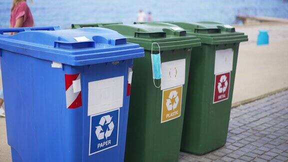 海滩上的垃圾分类容器人们在背景下经过地中海沿岸户外塑料垃圾桶上挂着用过的冠状病毒口罩缓慢的运动