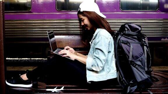 年轻的亚洲旅行女性背包使用笔记本电脑在火车站旅行