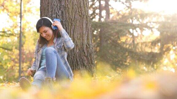倚靠在树上听音乐的年轻女子