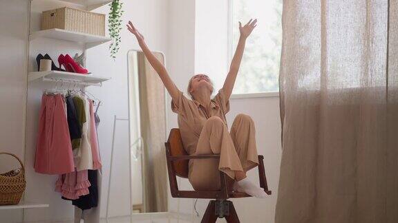 快乐的女人在试衣间的椅子上旋转举起双手
