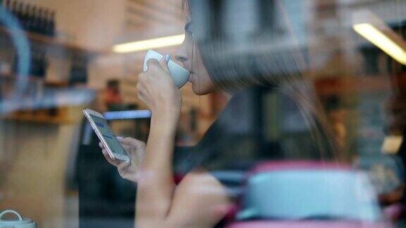 从大街上看一个留着长发的年轻女子正在用手机发短信喝着咖啡店里的白色杯子里的茶或咖啡
