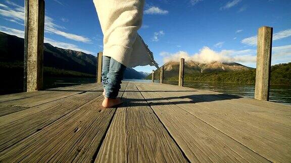 女人的脚在湖上的木栈桥上行走的特写