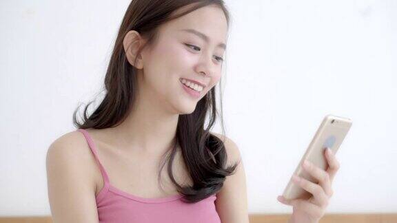 美丽的肖像年轻的亚洲女子微笑坐看智能手机阅读社交网络与享受在床上的卧室女孩聊天短信上网交流