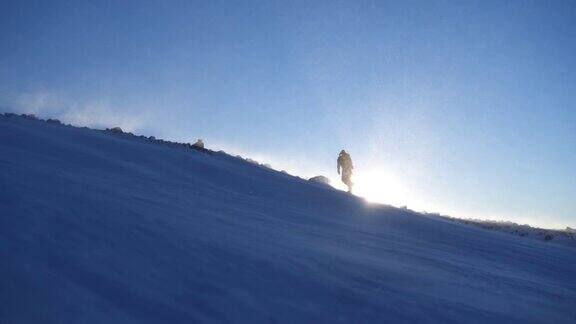 徒步旅行者爬上有积雪和阳光的山坡