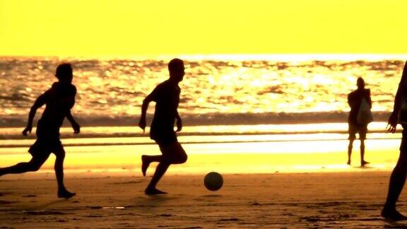 日落时分十几岁的孩子们在海边的沙滩上踢足球
