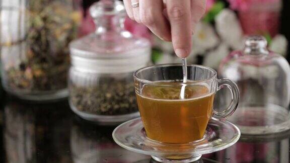 茶倒特写镜头将茶倒入透明的玻璃茶杯中下午茶时间透明玻璃茶壶和茶杯花草茶绿茶茉莉花茶把糖放在杯子里搅拌