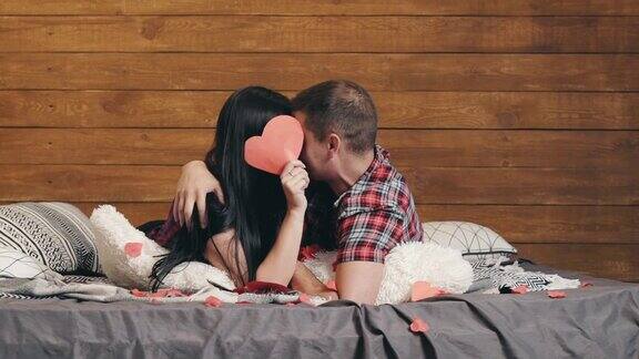 相爱的年轻情侣躺在床上互相拥抱、亲吻在室内用纸捂着脸