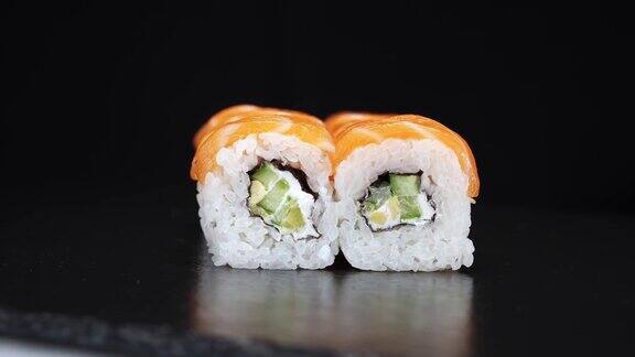 寿司卷在黑色背景上旋转近距离拍摄日本食物中的费城奶酪黄瓜和鲑鱼