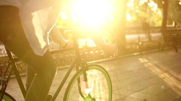 一个男人在早晨的公园或林荫大道骑自行车的近距离镜头一个骑自行车的年轻人的侧视图阳光照在背景上