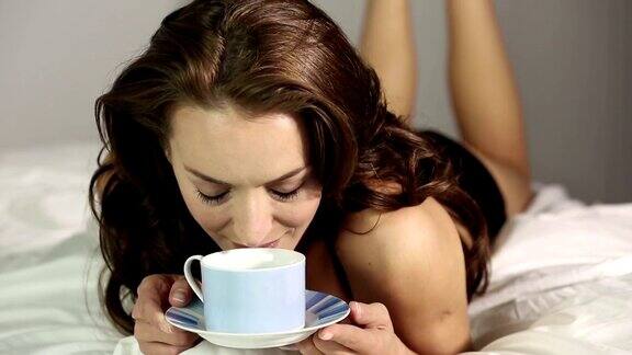 年轻女子在家里在床上喝咖啡