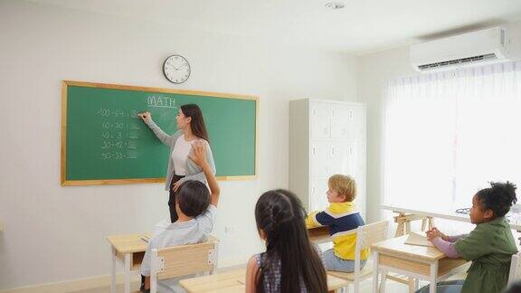 一群小学生在教室里跟着老师学习迷人美丽的女指导老师在幼儿园用快乐有趣的活动为幼儿讲解和教育