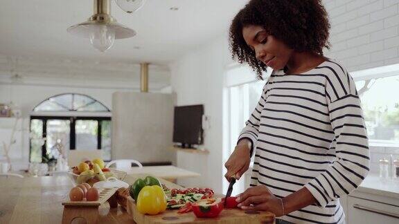 年轻女子独自在现代厨房里用切菜板上的刀切红甜椒