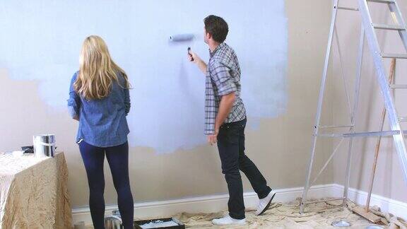 夫妇用油漆滚筒在墙上装饰房间