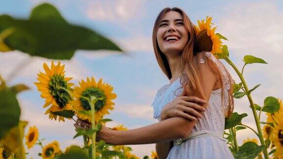 美丽的女孩摆姿势与向日葵的田野微笑夏天的风景是鲜花盛开从下到上的相机视图