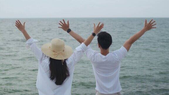 在假期的周末一对相爱的年轻夫妇举起手臂庆祝成功浪漫的情侣在海滩度假旅行