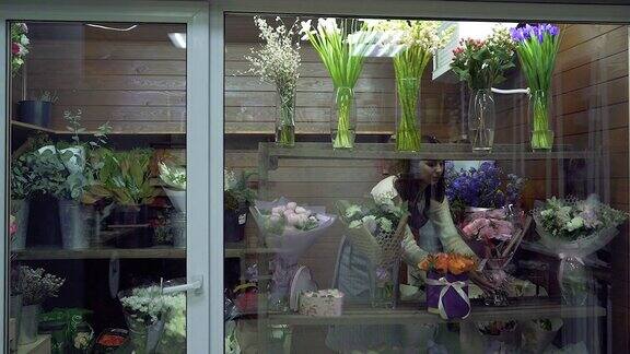 一名年轻女子花店店主正在整理花店冰箱窗户上的花束