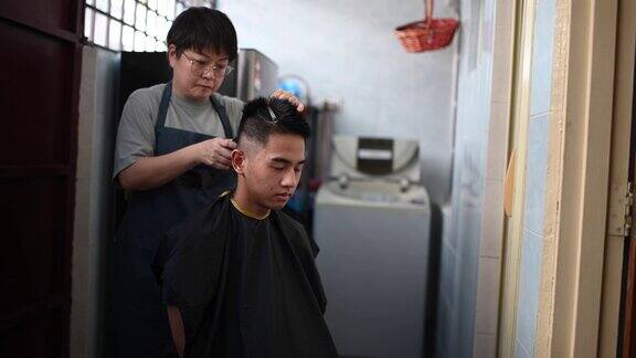 由于旅行禁令一名亚洲华人中年妇女正在厨房里为她的儿子修剪头发
