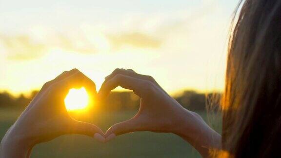 日落的心手在麦田里日出或日落时女人用手在太阳上画心形