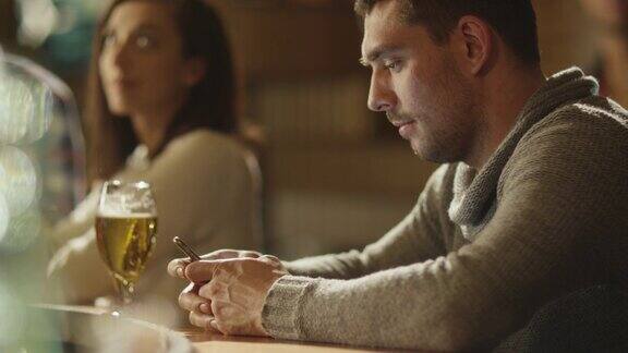 酒吧里一名男子正在用智能手机输入信息而柜台上放着一杯啤酒