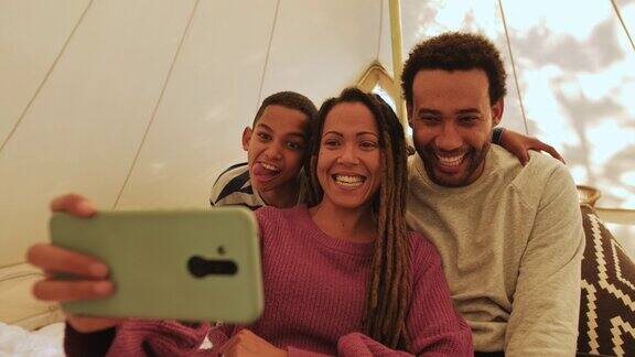 好玩的愚蠢的家庭做鬼脸在帐篷里用手机拍照