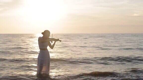 一个十几岁的女孩在日落的海滩上拉小提琴