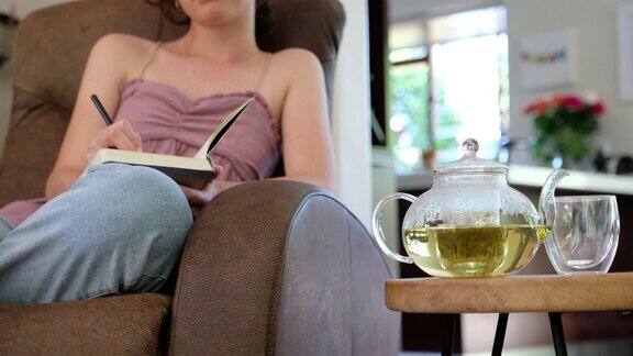 一名年轻女子一边写日记一边等着沏一壶茶